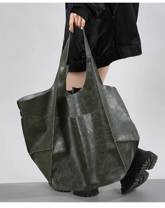 Detail shot of large vintage dark green leather tote bag held by a person in boots