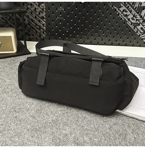 Detail of black techwear messenger bag featuring dual buckle straps and matte nylon fabric