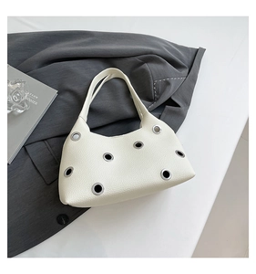 Detail view of cream-colored shoulder bag with silver eyelets and litchi grain leather texture