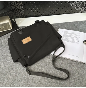 Close-up of black nylon messenger bag with buckle closure and leather brand logo