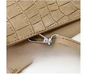 Detail of silver hardware hook and crocodile pattern texture on beige crossbody bag