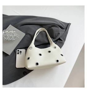Detail of white lychee leather texture and silver rivet eyelets on a modern shoulder bag