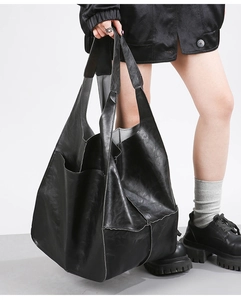 Close-up of black oversized soft leather tote bag with stylish contrast stitching on model