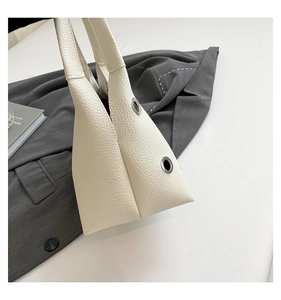 Detail of cream riveted hollow shoulder bag with lychee grain texture and silver eyelets