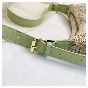 Dettaglio della tracolla in pelle verde chiaro con fibbia dorata su borsa in paglia intrecciata