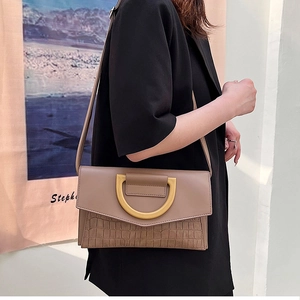 Detail of taupe crossbody bag with gold half-ring buckle and faux crocodile texture