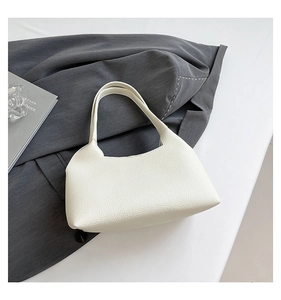 Close-up of cream rivets hollow shoulder bag in lychee textured leather on a grey blazer