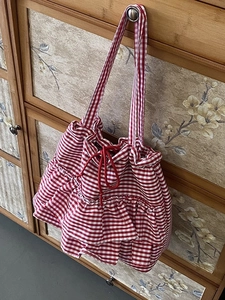 Floral plaid canvas tote bag with red drawstring and ruffled edges hanging on a wooden cabinet