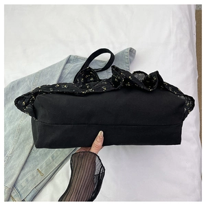 Detalle del volante floral en el bolso tote de lona negra con base de forma rectangular