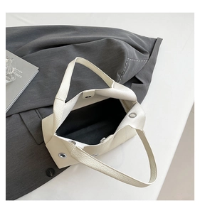 Macro view of cream shoulder bag featuring metal eyelets and premium lychee grain texture