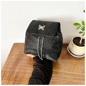 Close-up of black suede mini backpack featuring a silver butterfly clasp and chain tassels