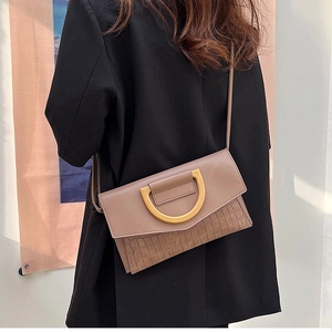 Detail of tan envelope crossbody bag with crocodile texture and gold D-ring hardware