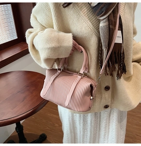 Detail of pink pleated handbag showing texture, round handle and shoulder strap