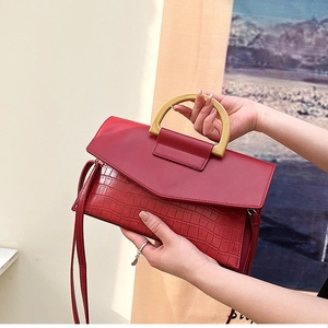 Detail of red crocodile embossed clutch bag with a yellow D-shaped handle and leather strap