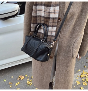 Detail of black pleated crossbody bucket bag with gold hardware in autumn street setting