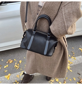 Detail of black pleated crossbody bag with gold hardware shown in a street style setting