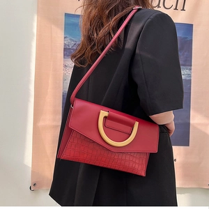 Detail of red crocodile texture handbag featuring a gold D-ring buckle and flap design