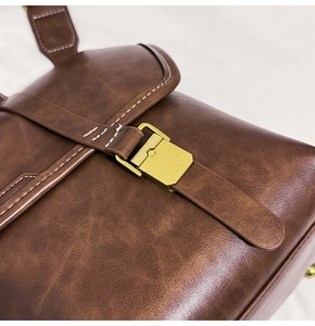 Close-up of brown vintage leather bag with gold metal clasp and white stitching details