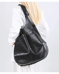 Detail of a black textured soft leather hobo bag worn by a model against a grey background
