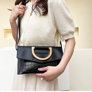 Detail of black faux leather crossbody bag with crocodile texture and D-ring buckle