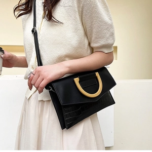 Detailed side view of black crocodile pattern crossbody bag with gold D-shaped handle