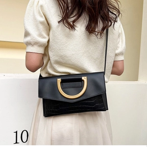 Detail of black crossbody bag with gold D-ring handle and faux crocodile texture