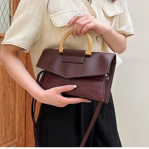 Detail of burgundy crocodile-embossed leather handbag with matte finish and arched handle