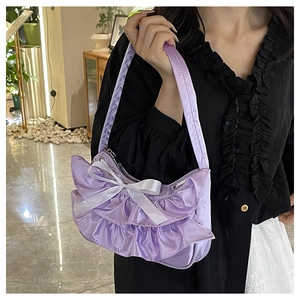 Detail of purple pleated underarm bag featuring a white silk bow and satin texture