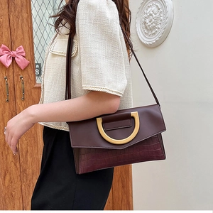 Detail of burgundy leather shoulder bag featuring crocodile texture and gold D-ring hardware