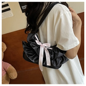 Detail of black satin shoulder bag featuring layered ruffles and a pink silk bow