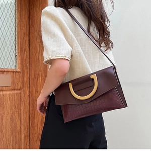 Detail of burgundy patchwork clutch with crocodile texture and gold D-shaped metal buckle