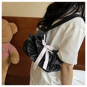 Detail of black satin shoulder bag featuring pink ribbon bow and ruffled side layering
