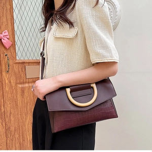 Detail of burgundy crocodile-embossed clutch with a unique wooden ring handle decor