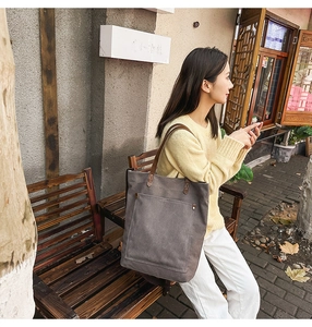 Detail of large dark grey canvas tote bag with brown leather handles in casual outdoor setting