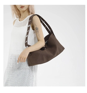 Detail of a brown canvas shoulder bag featuring a wide strap with silver metal eyelets