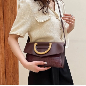 Detailed view of crocodile texture on burgundy clutch with gold D-ring handle and strap
