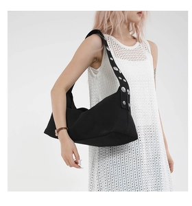 Detail of black canvas dumpling bag with silver grommets on a wide shoulder strap