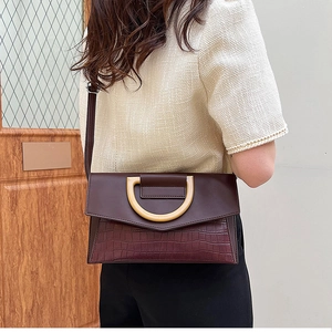 Detail of burgundy crocodile pattern crossbody bag with gold hardware on a female model