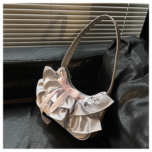 Detail of silver satin ruffled handbag with pink ribbon bow on black leather sofa