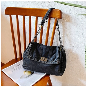 Detail einer Vintage Schultertasche aus schwarzem Denim mit Metallkette auf einem Holzstuhl
