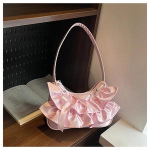 Detail of pink satin shoulder bag with ruffles and ribbon bows on a wooden shelf