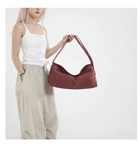 Close-up of a burgundy canvas hobo bag with metal eyelet strap on a model outfit