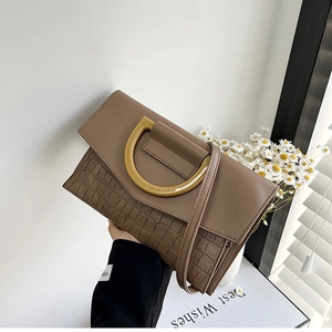 Detail of brown crocodile pattern handbag featuring a gold D-shaped handle and strap