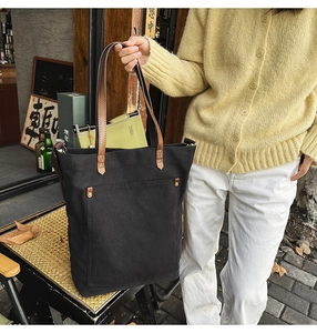 Macro shot of black canvas tote bag with brown leather handles and metal rivet detail