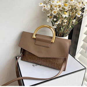 Detail of brown crocodile pattern handbag with amber circular handle on a pedestal
