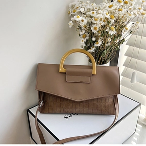 Detail of brown crocodile pattern handbag with rigid top handle on a white display box