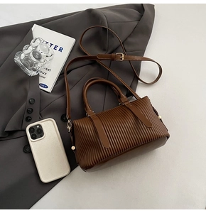 Close-up of dark brown pleated bucket bag with adjustable strap on a grey suit background