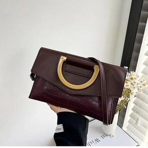 Detail of burgundy crocodile-patterned clutch with gold D-ring buckle and slim strap