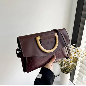 Detail of a brown crocodile pattern handbag featuring a stylish beige resin D-ring handle