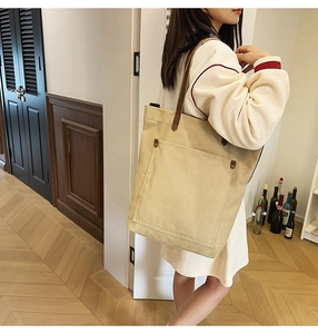 Detailed view of canvas tote bag with leather straps and front pocket worn by a model